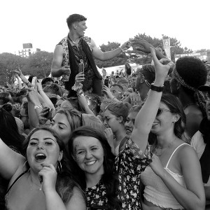 Festival crowd with their hands in the air, one person sitting on their friend’s shoulders